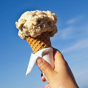 a hand holding an ice cream cone against a blue sky background